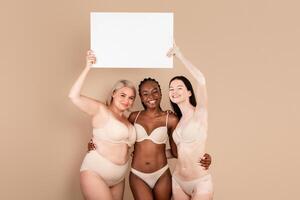 Group Of Multiracial Ladies In Underwear Posing With White Blank Placard, Diverse Body Positive Females Holding Signboard With Copy Space For Your Advertisement Or Motivational Inscription photo