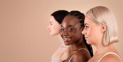 Profile Portrait Of Three Beautiful Body Positive Multiracial Women With Different Appearances Posing In Bra's Over Beige Background, Young African American Female Smiling At Camera, Copy Space photo