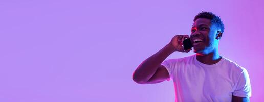 Happy young black man talking on smartphone in neon light, banner design with empty space. Cheerful African American guy making phone call, having conversation, enjoying communication photo