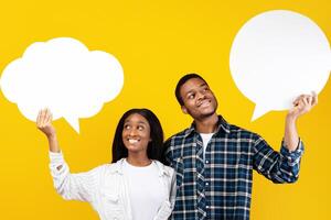 Different thoughts, dreams and empty place for words. Cheerful millennial african american couple of male and female holding abstract clouds with free space, isolated on yellow background, studio shot photo