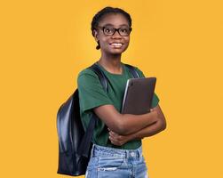 Smiling African Female Student Holding Laptop Hugging Computer Posing Standing On Yellow Studio Background. E-Learning And Educational Gadgets, Distant Online Study And Student's Lifestyle Concept photo