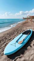A blue paddle board sits on the beach photo