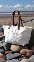 A white canvas bag with brown leather handles sitting on a rocky beach photo