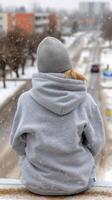 A person sitting on a ledge looking at a snowy road photo