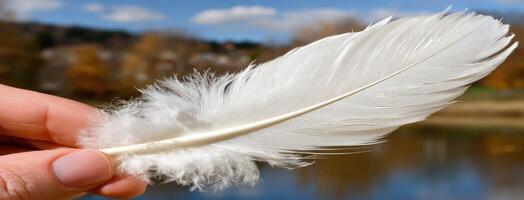 A person holding a white feather in front of a lake photo