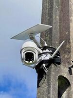 A security camera attached to a pole with a blue sky in the background photo