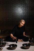 Woman practicing sound healing with singing bowls in a tranquil indoor space decorated with plants and soft lighting during a peaceful evening session.... photo
