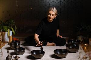 Woman practicing sound healing with singing bowls in a tranquil indoor space decorated with plants and soft lighting during a peaceful evening session.. photo