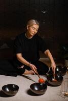 Woman practicing sound healing with singing bowls in a tranquil indoor space decorated with plants and soft lighting during a peaceful evening session... photo