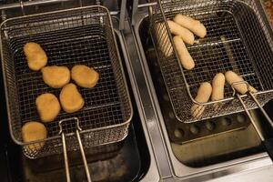 Fried snacks cooking in deep fryer with various shapes and sizes being prepared in a restaurant kitchen during busy afternoon hours photo