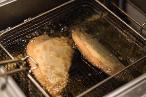 Crispy empanadas frying in hot oil in a restaurant kitchen during a busy evening service photo