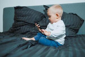 A toddler is comfortably engaged with a smartphone while nestled in a cozy bed, showcasing a blend of innocence, curiosity, and the interaction between childhood and modern technology photo