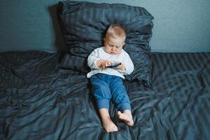 A young child can be seen fully engaged with a mobile device while comfortably relaxing on their bed, creating a delightful scene that captures the innocence and curiosity of childhood photo