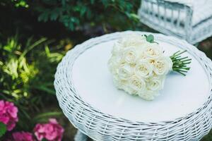 An Elegant White Rose Bouquet Arranged on a Wicker Table Set Within a Beautiful Garden Setting photo