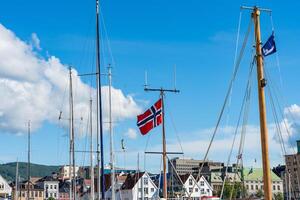 Bergen, Norway - July 9, 2024. Norwegian flag and yacht masts in harbor against clear blue sky photo