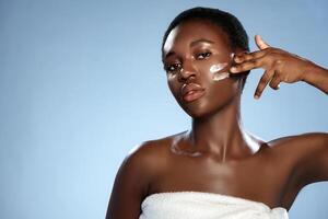 Woman applying skincare product on her face in a studio with blue background during daylight hours photo