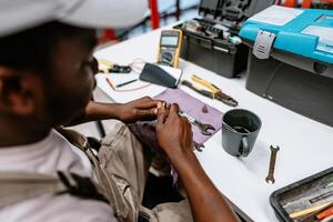 Technician repairs tools in workshop while sitting at desk with various instruments and materials photo