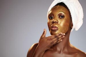 Woman applying a gold facial mask while wrapped in a towel showcasing skincare routines in a clean indoor setting photo