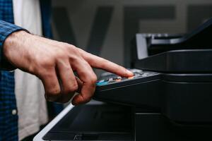 Person uses a multifunction printer to operate photocopying or scanning functions in an office setting during daylight hours photo