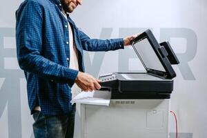 Man using a photocopier in a modern office space while preparing documents for printing photo