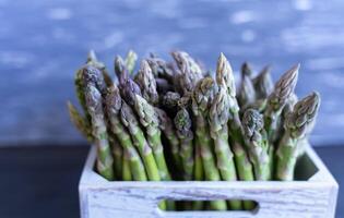 Crisp green asparagus piled in a gray wooden crate against contrasting gray background perfectly fresh and ready for spring recipes photo