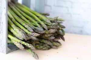 Crisp green asparagus spears falling out of a rustic gray wooden crate on a neutral background photo