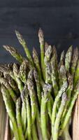 Top-down photo of green asparagus stalks arranged in a crate on a dark wooden surface for a farm-fresh feel