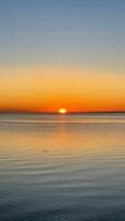 Beautiful sunset over the sea. The sun sets on the water. The sky is painted with bright colors. Summer evening. Sunset beach. Vertical photo