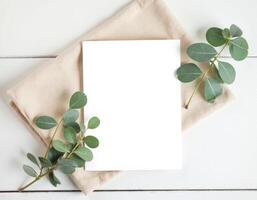 Blank paper with eucalyptus leaves on white wooden table photo