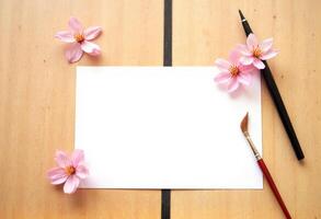 A blank sheet of paper, a paint brush and a flower on a wooden table photo