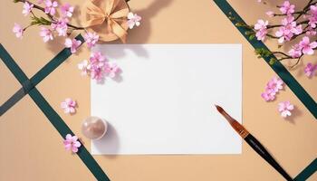 A blank sheet of paper, a paintbrush and a branch of cherry blossoms on a brown photo