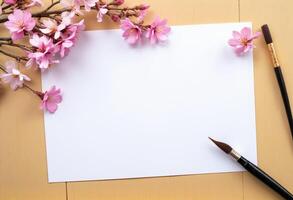 A blank sheet of paper, a paint brush and a cherry blossom branch on a wooden table photo