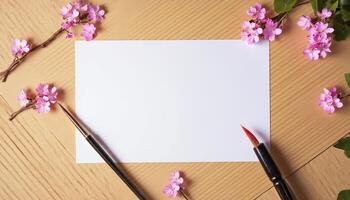 A blank sheet of paper, paint brushes and a branch of pink flowers on a wooden table photo