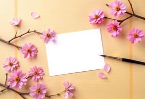Pink flowers and paper on yellow background with blank space for text photo