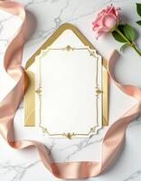 An envelope with a gold frame and pink rose on a marble surface photo