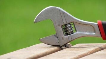 Adjustable wrench resting on wooden surface during bright daylight in a garden setting photo