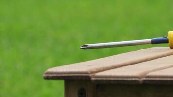 Close-up view of a screwdriver resting on a wooden table in a green outdoor setting during daylight photo