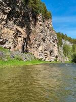 A beautiful and serene river is flowing gently through a stunning canyon, with a majestic cliff rising prominently in the background, creating a picturesque natural landscape photo