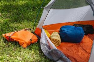 Experience a cozy camping setup featuring colorful gear placed inside a tent on lush green grass, ideal for a perfect outdoor escape. Embrace the warmth of nature while enjoying leisure time photo