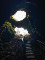 There is a mysterious cave with stairs that lead up to its entrance, and a soft light glowing from within it, illuminating the dark surroundings just outside the caves mouth photo