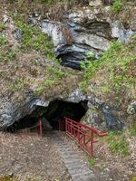 A fascinating cave features a set of stairs leading right down into it, complemented by a bright red railing that provides safety and support for those who dare to explore photo