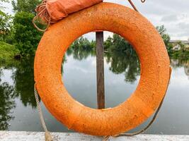 An orange life preserver, often used for safety, is currently hanging on a sturdy pole that is positioned conveniently near a large body of water where people can swim and relax photo