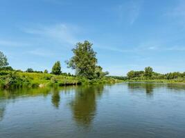 On a bright and sunny day, a sparkling body of water is beautifully framed by vibrant green trees, while it is surrounded by a rich and colorful landscape that captivates the eye photo