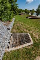 A manhole cover can be seen currently resting in the grass right next to a sturdy rock wall, creating a unique and interesting contrast between natures beauty and urban infrastructure photo