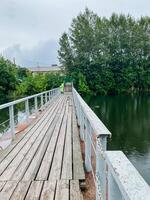 A charming wooden bridge gracefully spans over a tranquil body of water, surrounded by lush trees that provide shade and beauty to the scene, creating a picturesque landscape photo