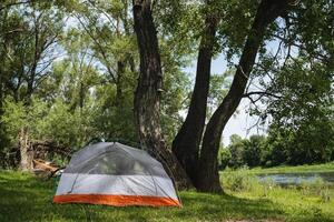 This peaceful campsite by a flowing river has a cozy tent under a lovely tree canopy, ideal for relaxation and outdoor activities in a beautiful setting with stunning scenery and lush greenery photo