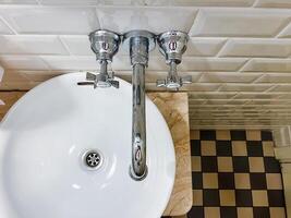 In this bathroom, there is a unique sink featuring three distinct faucets, complemented by an eyecatching checkered floor design that enhances the overall aesthetic appeal of the space photo