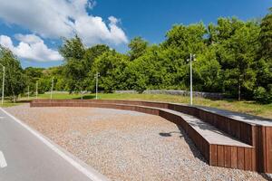 A beautifully crafted wooden bench is situated on the side of a winding road within the serene confines of a park, offering a perfect resting spot for visitors enjoying natures beauty photo