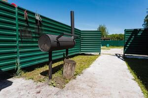 In a serene backyard, a sleek black grill stands out among lush green fencing, inviting summer cooking and relaxation under a clear blue sky, perfect for gatherings with friends and family photo