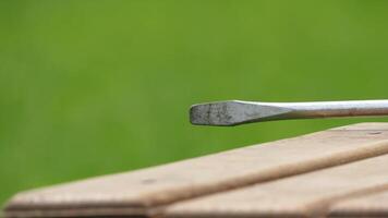 Close-up view of a metal tool resting on a wooden surface in a green outdoor setting during daylight photo